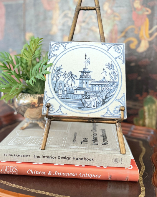 Blue-and-white Minton Chinoiserie tile displayed on a brass easel above stacked design books