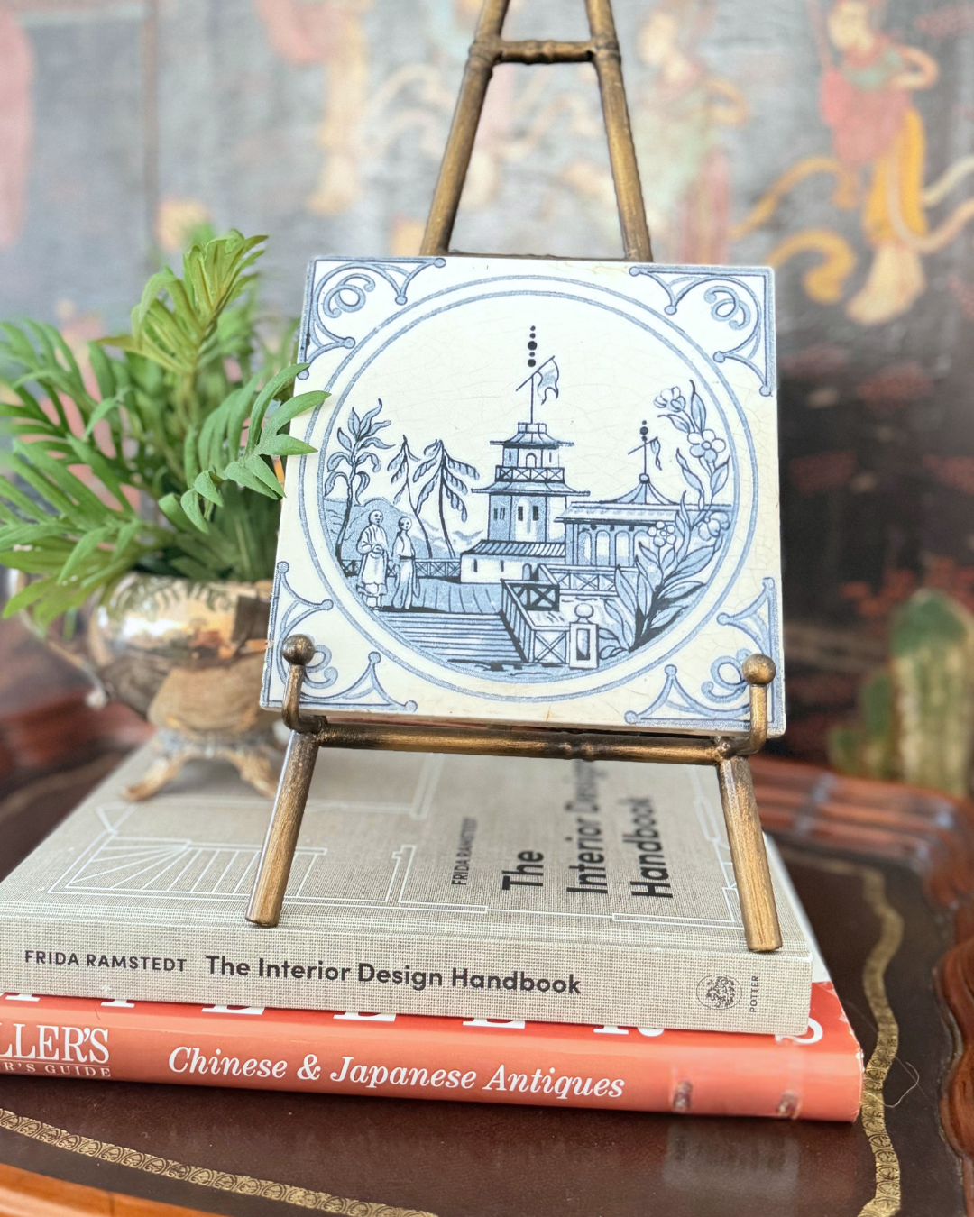 Blue-and-white Minton Chinoiserie tile displayed on a brass easel above stacked design books