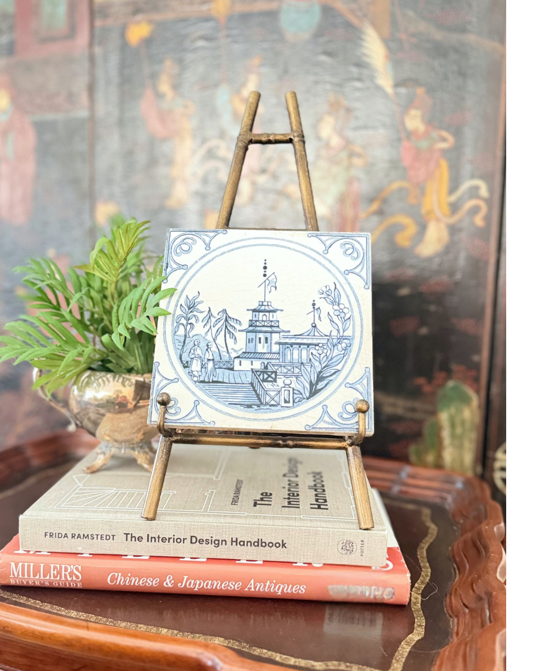 Antique Minton blue-and-white Chinoiserie pavilion tile displayed on a brass easel with design books and fern.