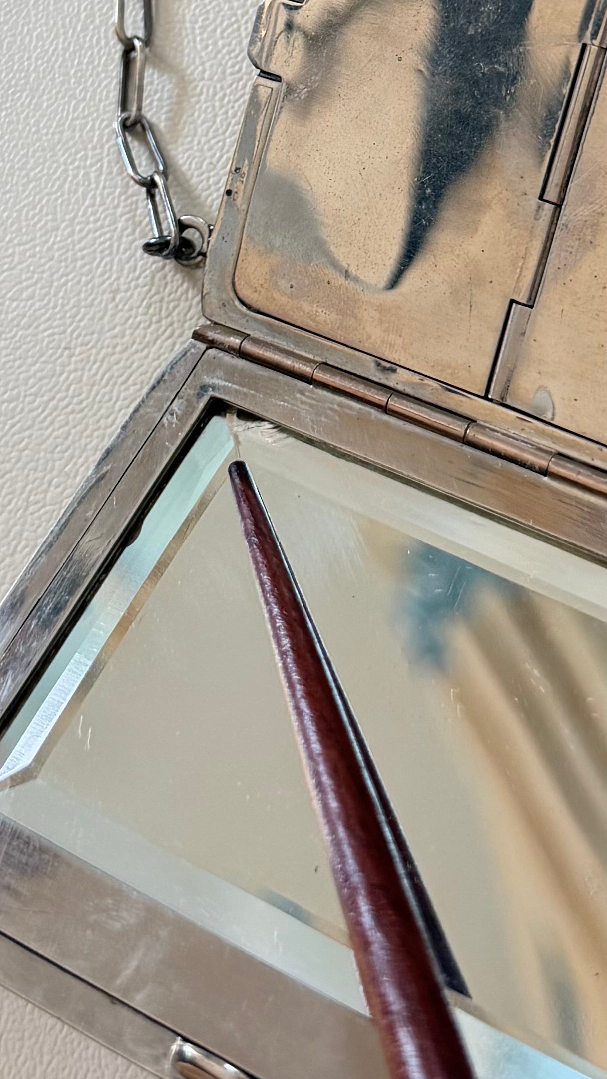 Close-up of beveled mirror in antique German-silver dance purse with pointer indicating a small edge chip.