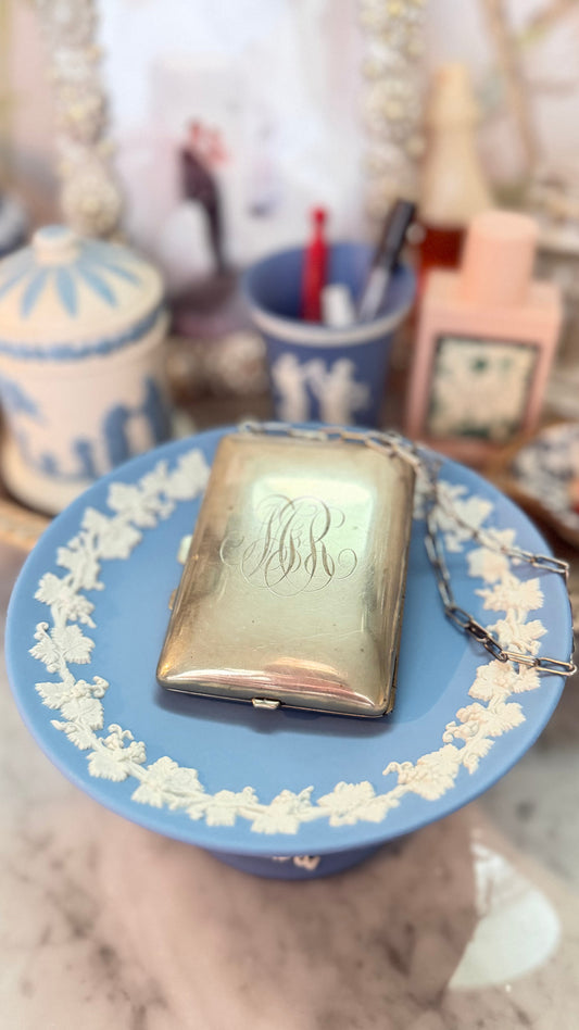 Antique German-silver dance purse with engraved script monogram and chain displayed on a blue Wedgwood pedestal.