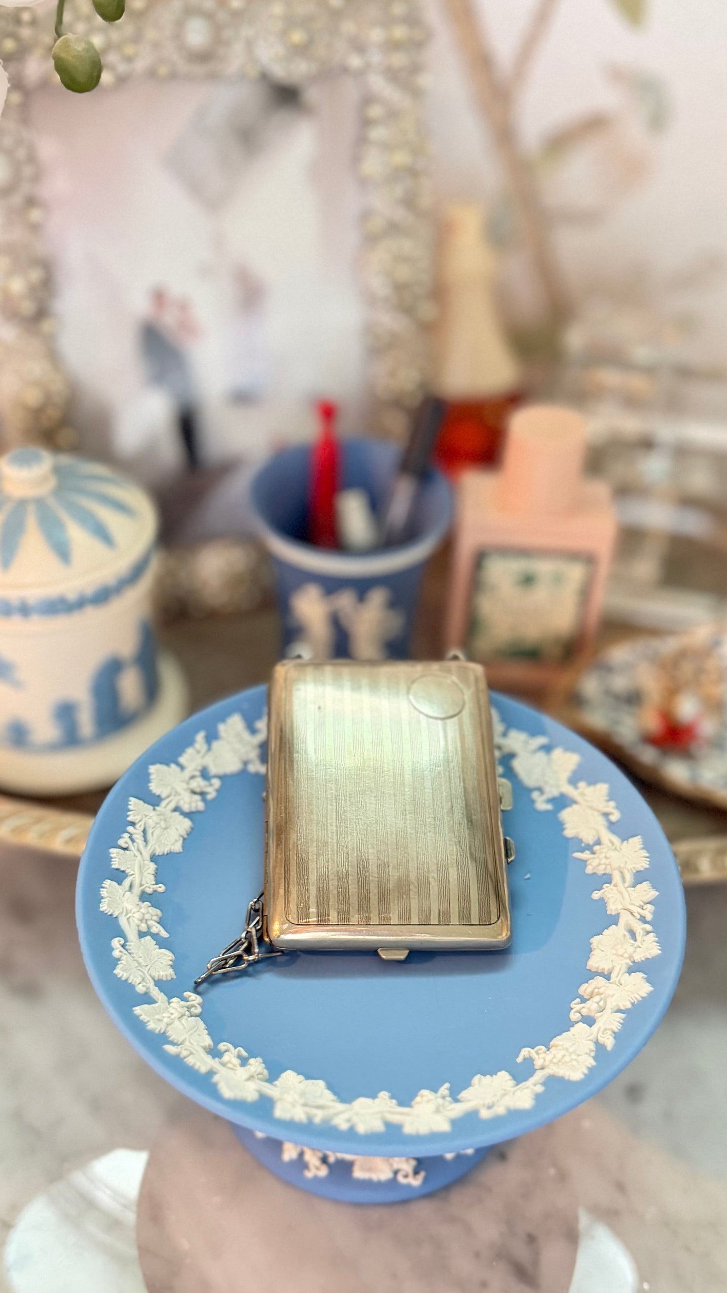 Back of antique German-silver dance purse with vertical engine-turned stripes, circular cartouche, and attached chain on a blue Wedgwood pedestal.